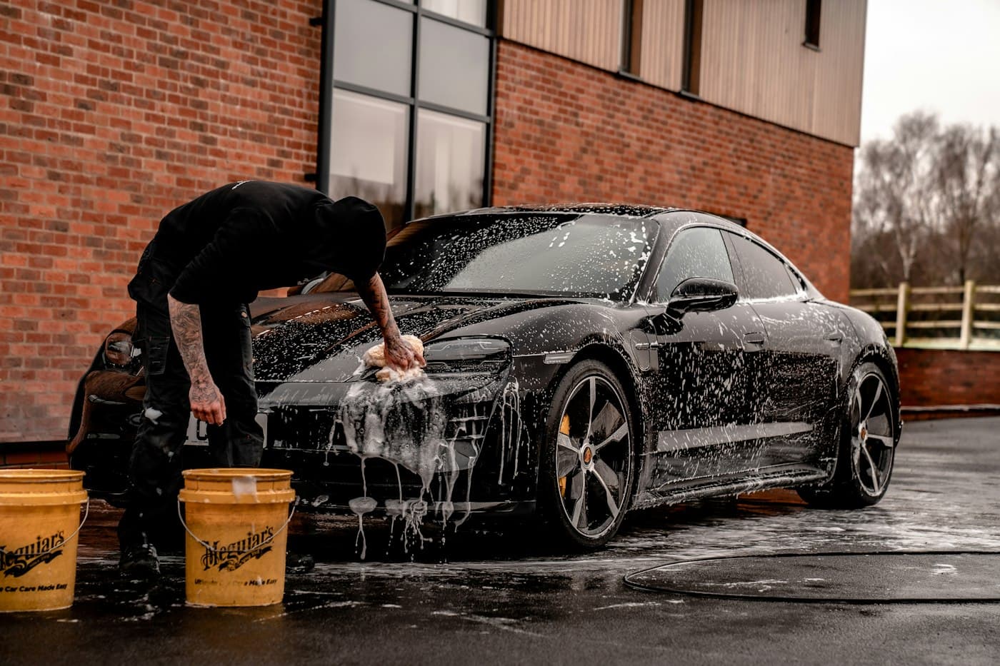 A detailer washing a foam-covered car with a wash mitt.