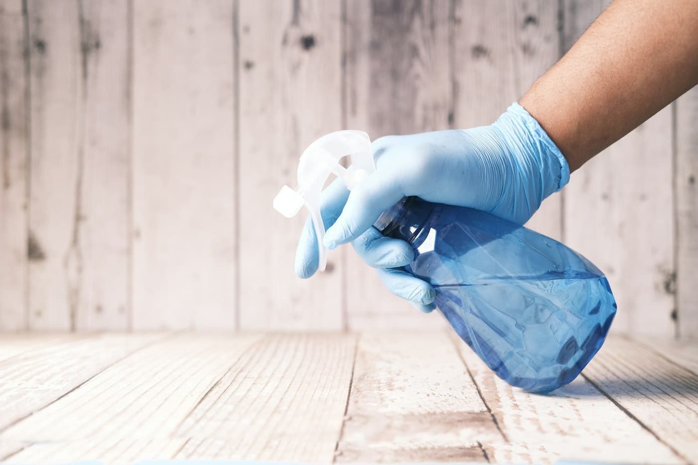 A gloved hand holding a spray bottle over a wooden surface.
