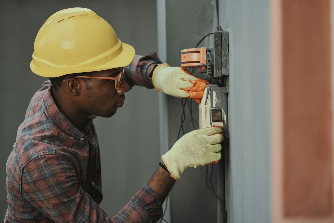 An electrician in a hard hat wiring an outdoor electrical box.