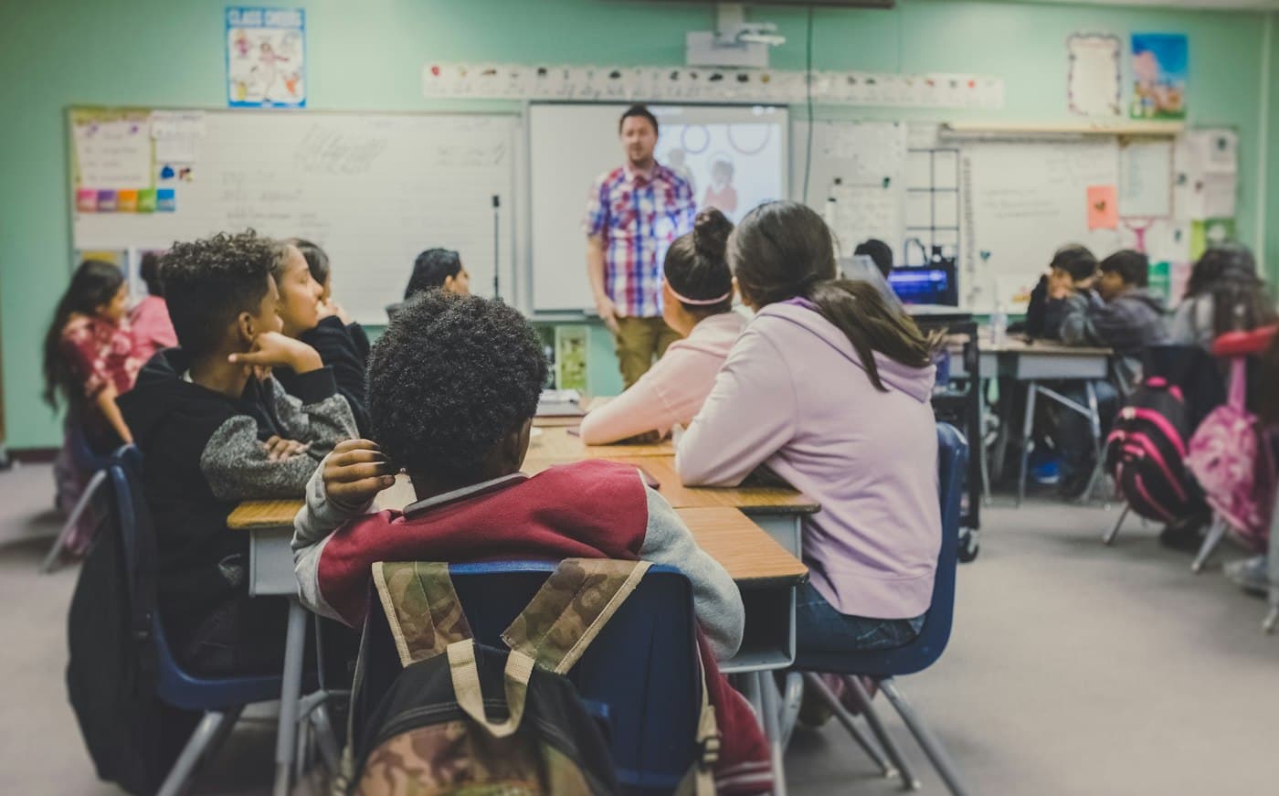 Students seated at desks facing a teacher at the whiteboard.